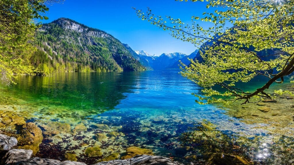 Klarer Bergsee mit Blick auf bewaldete Hänge und ferne Gipfel